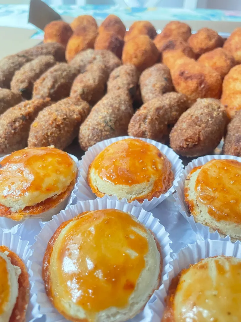A close view of quibes and risoles beside glazed empadinhas in paper cases