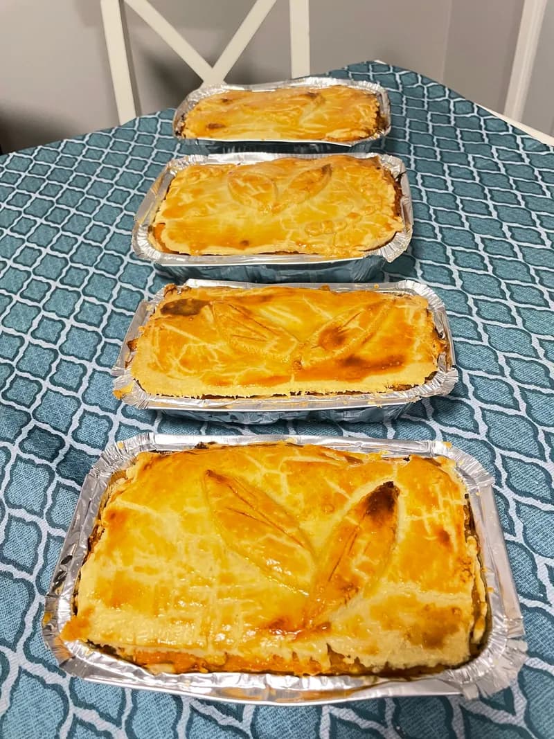 Four empadões in foil trays, smallest to largest, their pastry lids glazed and scored